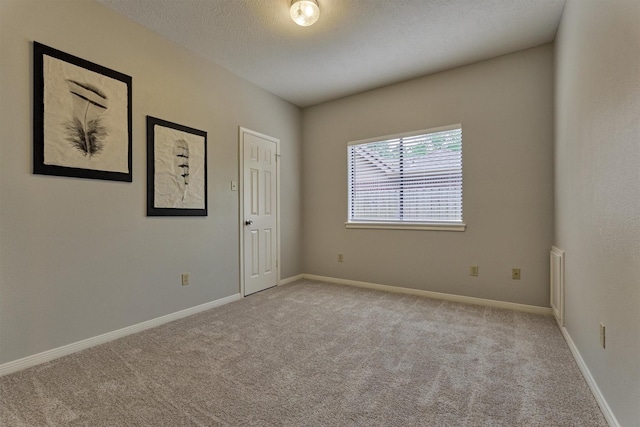 empty room with carpet floors, a textured ceiling, and baseboards