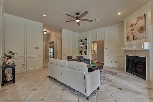 living area featuring visible vents, a decorative wall, a tile fireplace, a ceiling fan, and light tile patterned floors