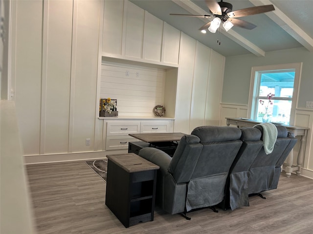 living area featuring ceiling fan, wainscoting, beam ceiling, a decorative wall, and wood finished floors