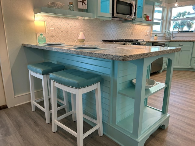 kitchen featuring open shelves, wood finished floors, a breakfast bar area, tasteful backsplash, and stainless steel appliances