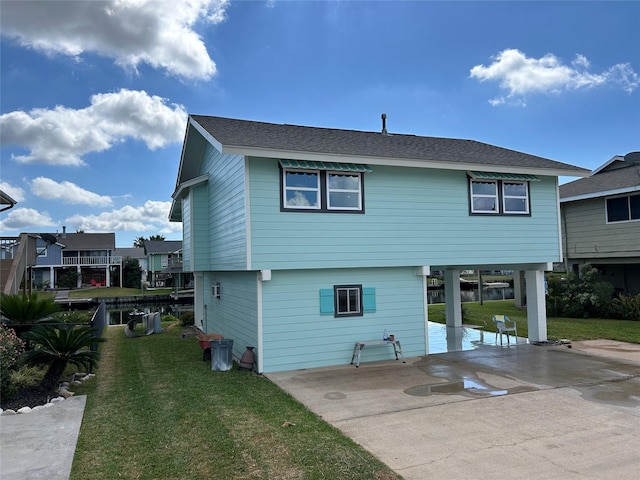 rear view of house featuring roof with shingles, concrete driveway, a patio area, a carport, and a yard