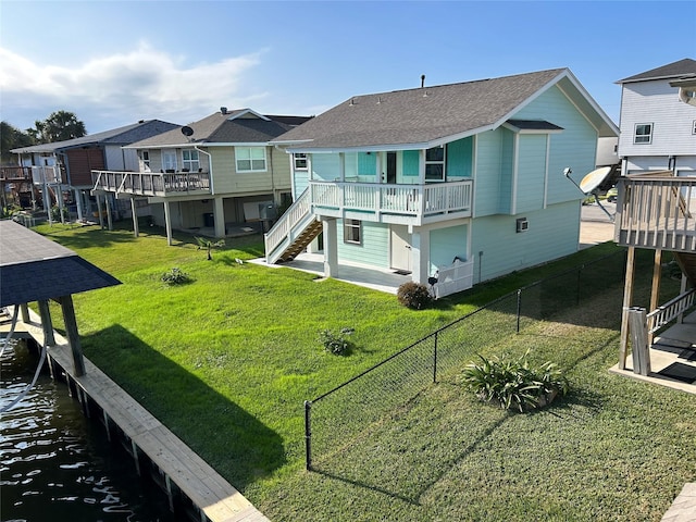 rear view of house featuring a deck with water view, a fenced backyard, roof with shingles, a yard, and stairway