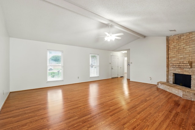 unfurnished living room with a brick fireplace, light wood-style floors, ceiling fan, vaulted ceiling with beams, and a textured ceiling