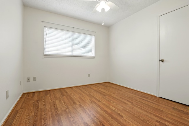 spare room with baseboards, ceiling fan, light wood finished floors, and a textured ceiling