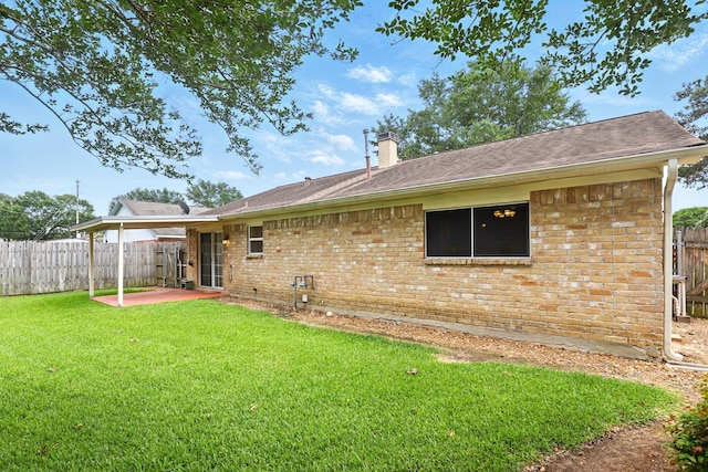 rear view of house featuring fence, a patio, a chimney, brick siding, and a lawn
