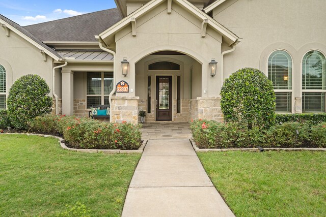 entrance to property featuring a yard, covered porch, stone siding, and stucco siding