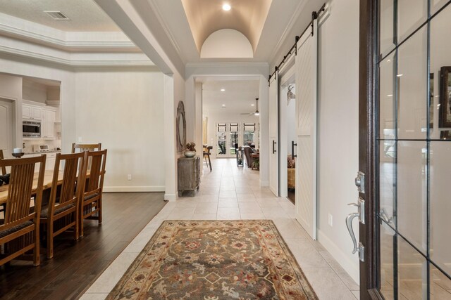 entrance foyer featuring visible vents, ornamental molding, baseboards, a barn door, and light wood finished floors