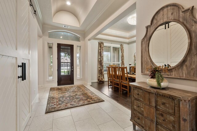 tiled entryway featuring baseboards, ornamental molding, vaulted ceiling, and visible vents