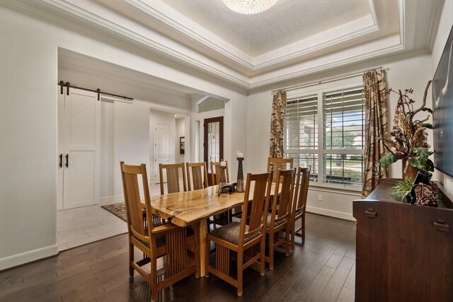 dining space featuring crown molding, a barn door, baseboards, a tray ceiling, and dark wood-type flooring
