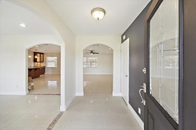foyer featuring baseboards, a ceiling fan, arched walkways, and light tile patterned flooring