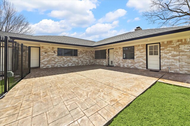 back of house featuring a chimney, roof with shingles, brick siding, fence, and a patio
