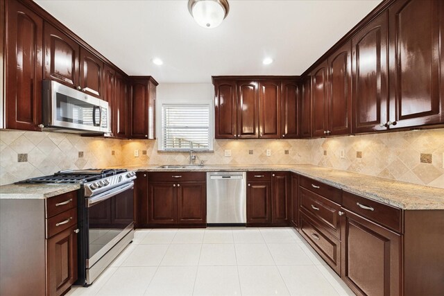 kitchen featuring decorative backsplash, light stone counters, a sink, light tile patterned floors, and stainless steel appliances