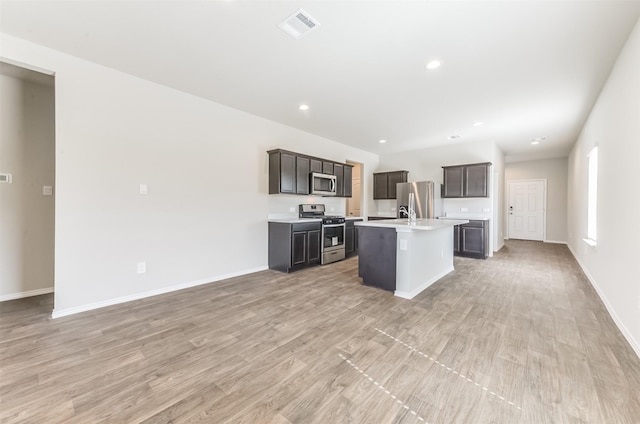 16524 Cascading Pines Ct, Conroe, TX 77302 - kitchen with visible vents, a kitchen island with sink, light countertops, light wood finished floors, and appliances with stainless steel finishes
