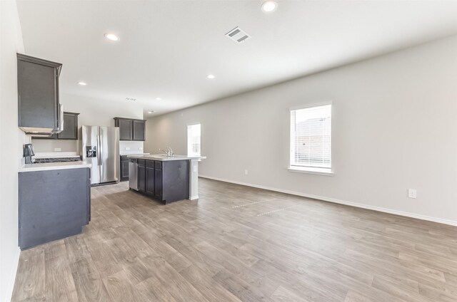 16524 Cascading Pines Ct, Conroe, TX 77302 - kitchen featuring visible vents, light wood-style floors, a center island with sink, light countertops, and stainless steel appliances
