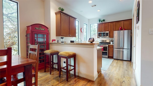kitchen featuring brown cabinetry, stainless steel appliances, light wood-type flooring, and visible vents