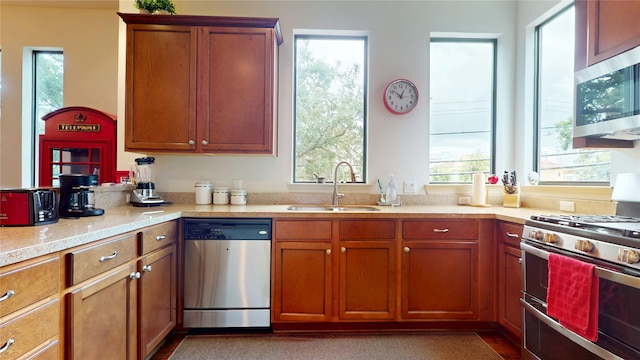 kitchen featuring a sink, appliances with stainless steel finishes, light stone countertops, and brown cabinets