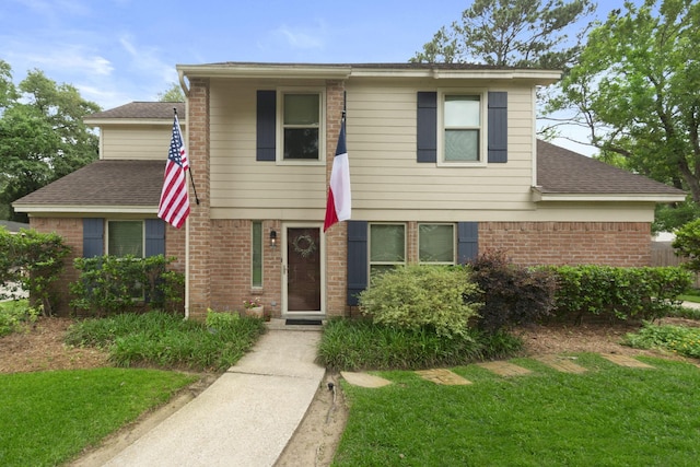 traditional home with brick siding, a shingled roof, and a front lawn