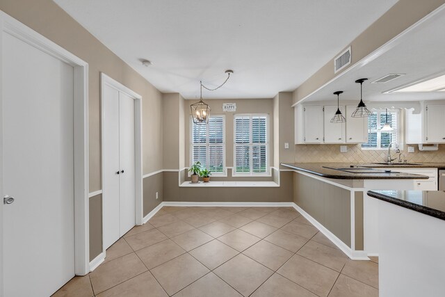 kitchen with white cabinets, dark countertops, a sink, tasteful backsplash, and visible vents