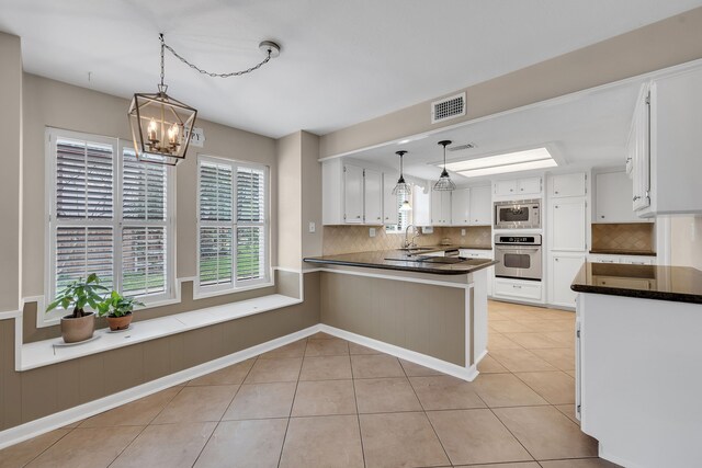 kitchen featuring visible vents, built in microwave, a sink, a peninsula, and stainless steel oven