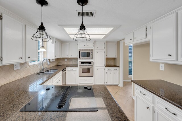 kitchen with visible vents, dark stone counters, white cabinets, a sink, and appliances with stainless steel finishes