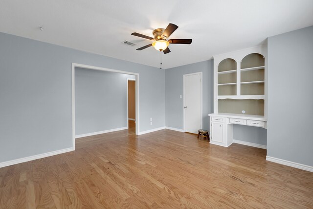unfurnished living room featuring visible vents, light wood-style floors, baseboards, built in desk, and a ceiling fan
