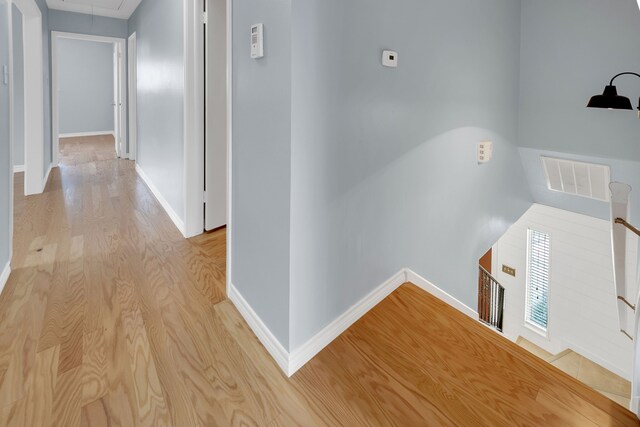 hallway featuring baseboards, attic access, wood finished floors, and an upstairs landing