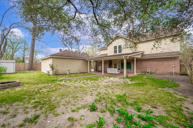 back of house with fence, brick siding, a patio, a yard, and a fire pit