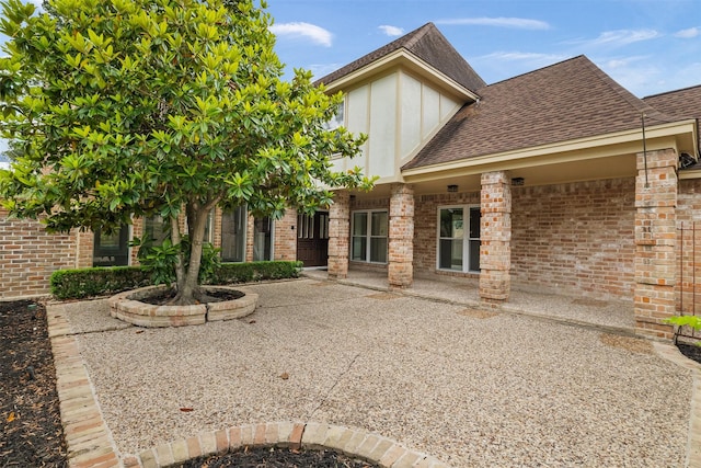 rear view of house featuring roof with shingles, a patio, and brick siding