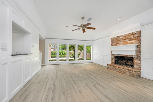 unfurnished living room featuring a fireplace, a decorative wall, a ceiling fan, light wood-type flooring, and visible vents