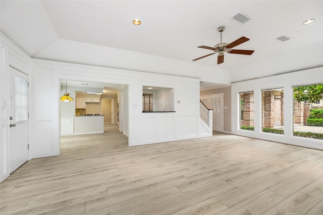 unfurnished living room featuring stairway, a ceiling fan, a decorative wall, and visible vents
