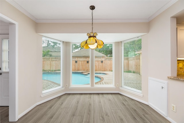 unfurnished dining area with an inviting chandelier, ornamental molding, baseboards, light wood finished floors, and a wealth of natural light