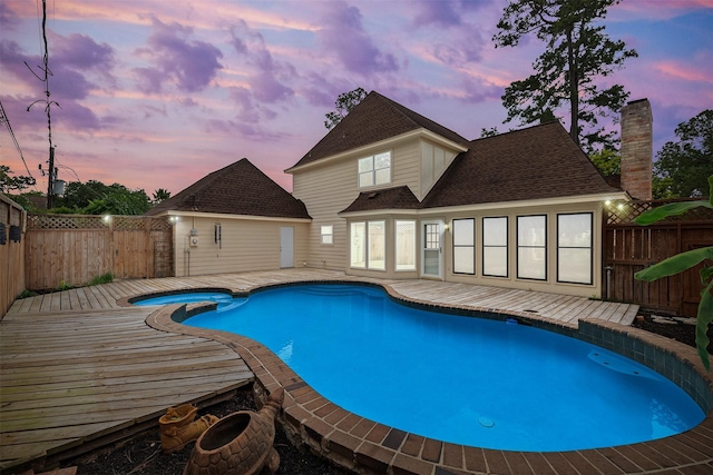 pool at dusk with a fenced backyard, a wooden deck, and a pool with connected hot tub