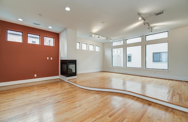402 Parker St, Houston, TX 77007 - unfurnished living room featuring visible vents, baseboards, light wood-type flooring, rail lighting, and a multi sided fireplace