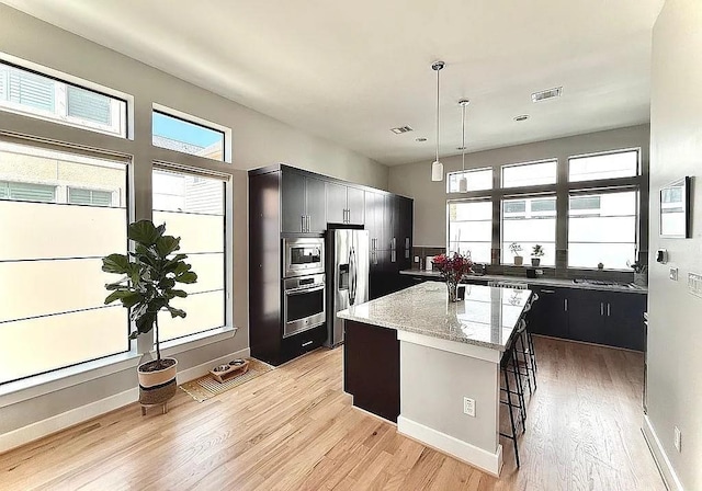 kitchen featuring visible vents, a center island, light stone counters, light wood finished floors, and stainless steel appliances