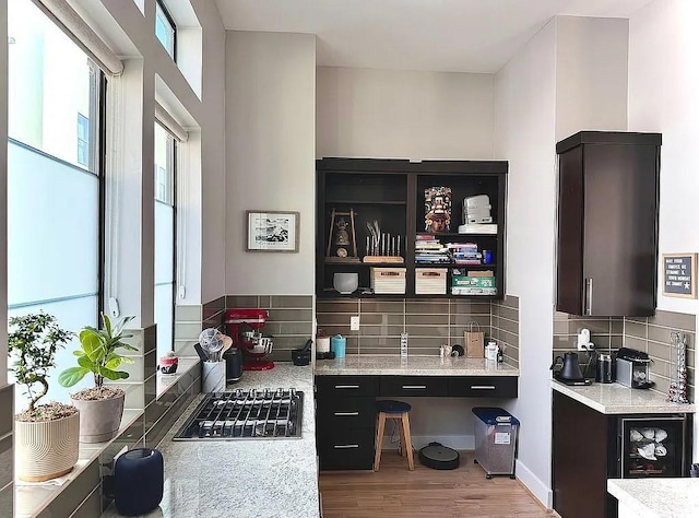 bar featuring backsplash, stainless steel gas stovetop, a healthy amount of sunlight, and light wood-style flooring