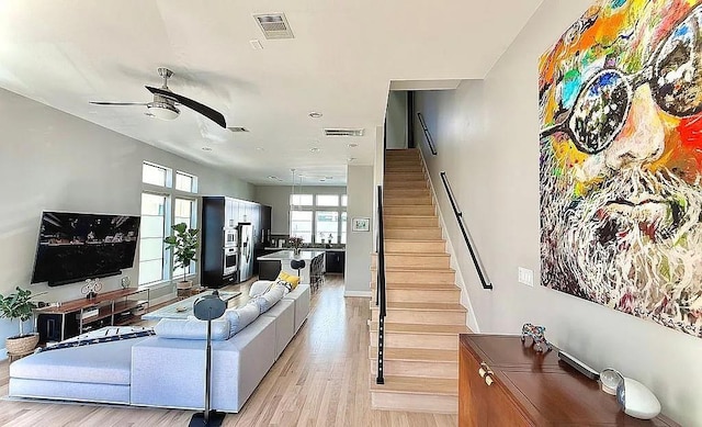 living area featuring ceiling fan, visible vents, stairway, and light wood-style floors