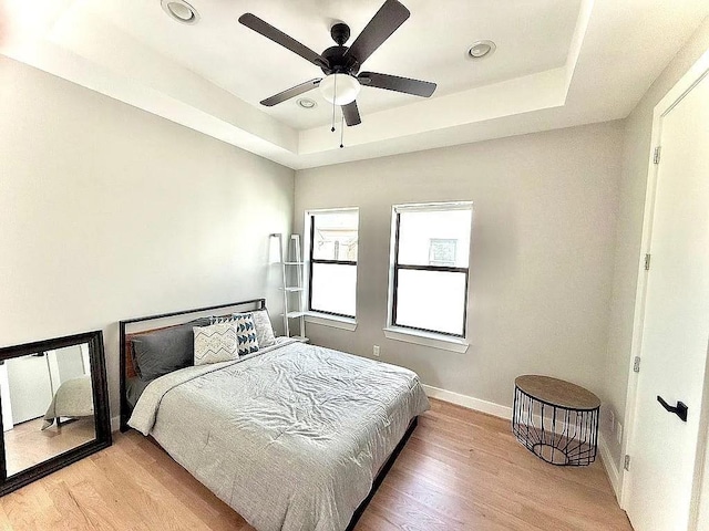 bedroom with a raised ceiling, baseboards, recessed lighting, and light wood-style flooring