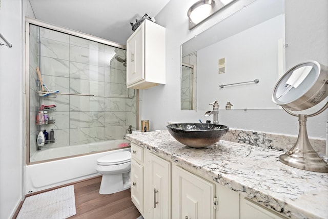 bathroom with visible vents, vanity, wood finished floors, toilet, and enclosed tub / shower combo