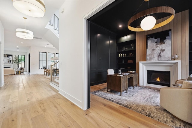 interior space featuring built in features, baseboards, light wood finished floors, a glass covered fireplace, and recessed lighting