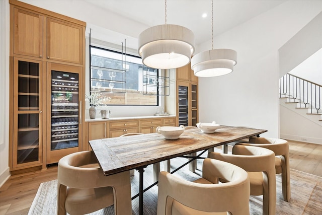 dining area featuring light wood-style floors, stairs, baseboards, and beverage cooler