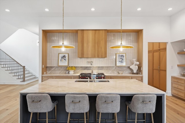 kitchen with decorative backsplash, light wood-style flooring, a breakfast bar area, and a kitchen island with sink