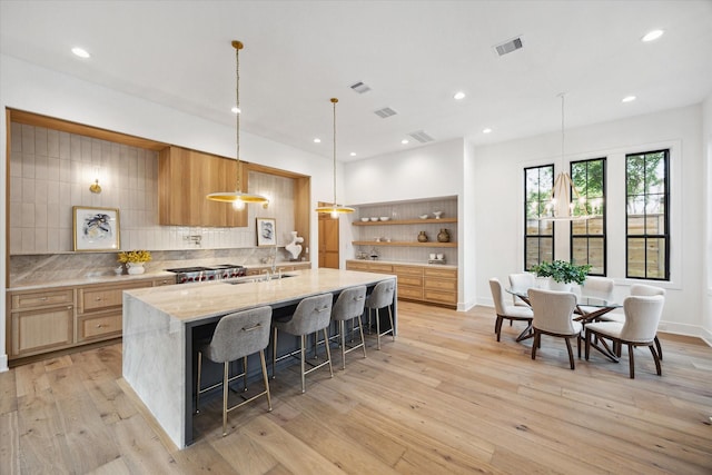 kitchen with visible vents, open shelves, tasteful backsplash, a large island with sink, and a sink