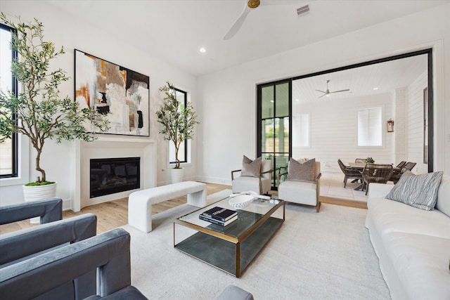 living area with a glass covered fireplace, a ceiling fan, light wood finished floors, and visible vents