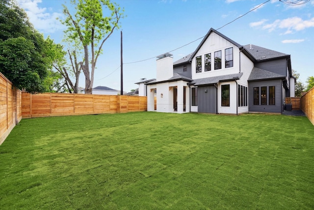 back of house with a lawn, a fenced backyard, board and batten siding, and roof with shingles