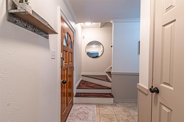 stairs with a wainscoted wall, ornamental molding, and tile patterned floors