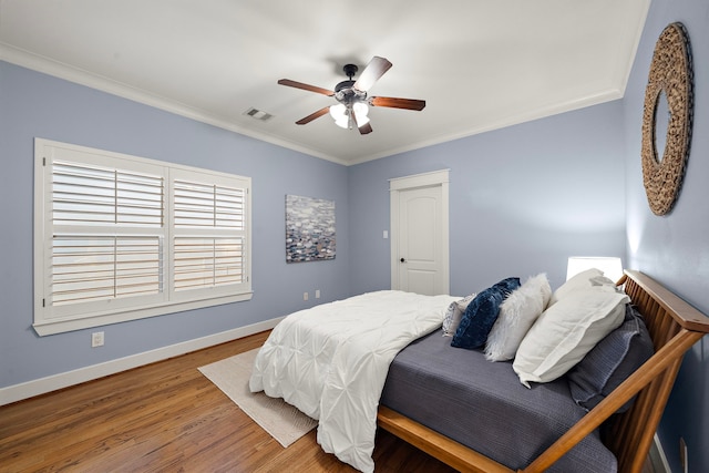 bedroom featuring ceiling fan, visible vents, crown molding, wood finished floors, and baseboards