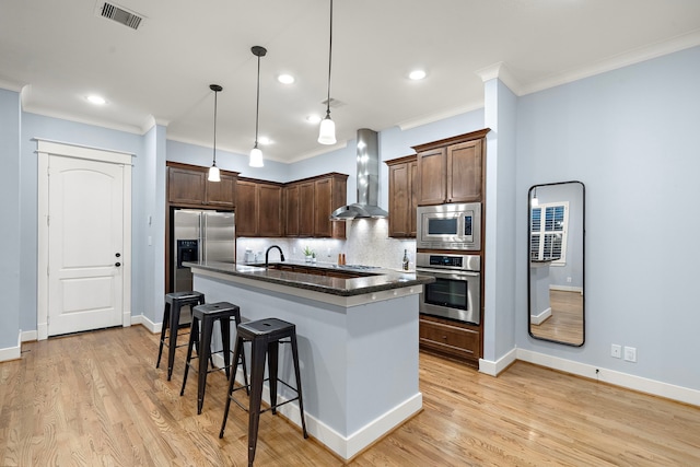 kitchen featuring wall chimney range hood, crown molding, appliances with stainless steel finishes, a kitchen breakfast bar, and visible vents