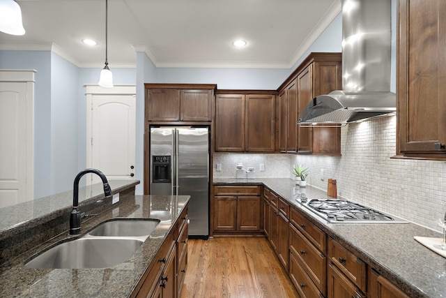 kitchen featuring appliances with stainless steel finishes, hanging light fixtures, light wood-type flooring, a sink, and wall chimney exhaust hood