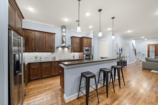 kitchen featuring crown molding, wall chimney exhaust hood, a breakfast bar, and stainless steel appliances