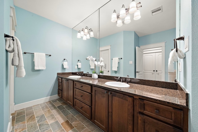bathroom featuring baseboards, a sink, stone finish flooring, and double vanity